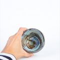 havaneser.shop Galaxy Glaze Becher aus Keramik mit blau-grün-brauner Verlaufglasur in einer Hand gehalten