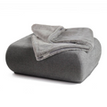 havaneser.shop Wohndecke aus grauem Webpelz und weichem Fleece, elegant gefaltet auf einem passenden Sitzhocker