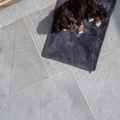 havaneser.shop Hundedecke aus weichem Webpelz in Grau, auf der ein kleiner brauner Hund auf Steinfliesen liegt.